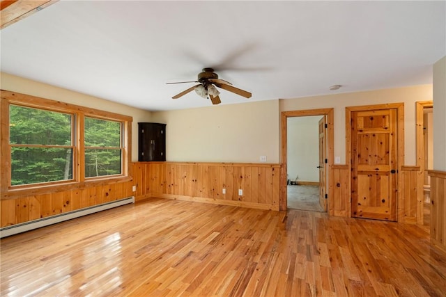 empty room featuring ceiling fan, light hardwood / wood-style floors, baseboard heating, and wooden walls