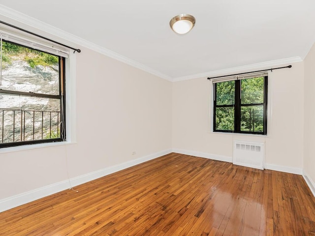 empty room featuring wood-type flooring, ornamental molding, and radiator