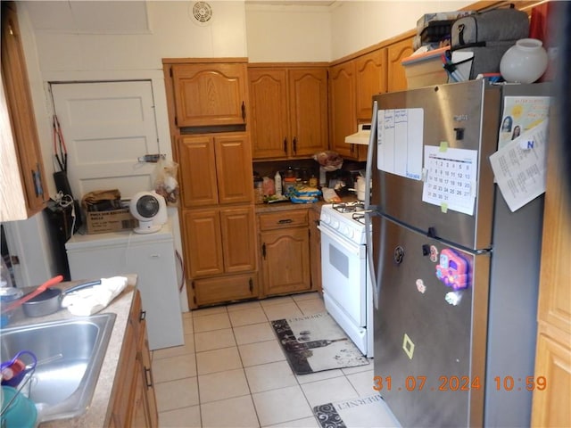 kitchen featuring washing machine and clothes dryer, ventilation hood, stainless steel fridge, light tile patterned floors, and white gas range oven