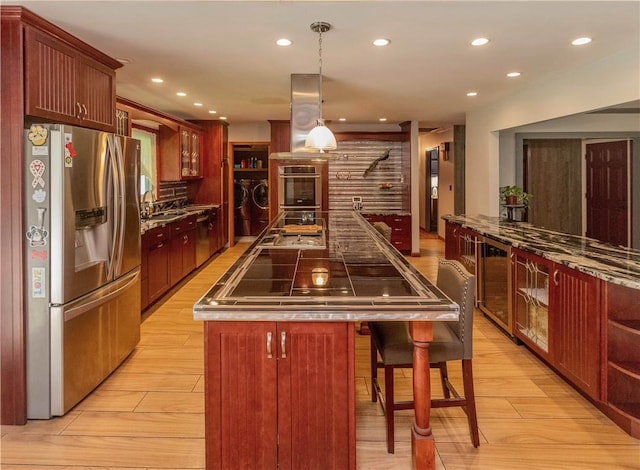 kitchen with stainless steel appliances, washer and dryer, pendant lighting, light hardwood / wood-style floors, and a kitchen island