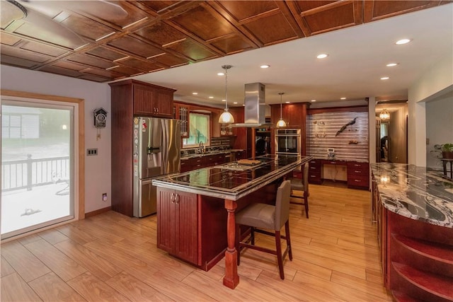 kitchen with island exhaust hood, appliances with stainless steel finishes, a breakfast bar, light hardwood / wood-style flooring, and hanging light fixtures