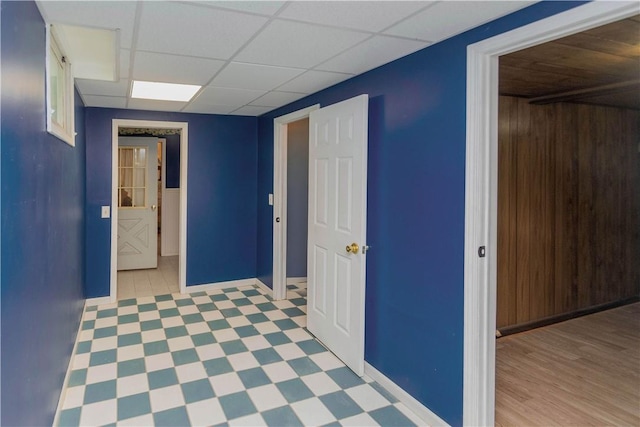 hallway with a paneled ceiling, light wood-type flooring, and wooden walls