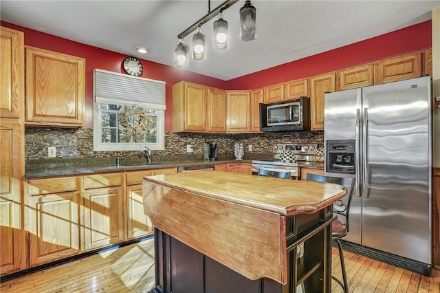 kitchen with stainless steel appliances, backsplash, decorative light fixtures, a kitchen island, and light wood-type flooring