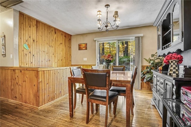 dining room with wood walls, crown molding, a chandelier, light hardwood / wood-style floors, and a textured ceiling