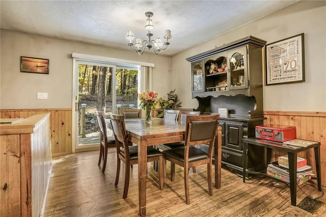 dining space with hardwood / wood-style floors, a textured ceiling, wooden walls, and a chandelier