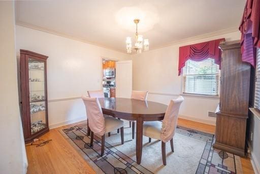 dining space featuring crown molding, wood-type flooring, and a notable chandelier