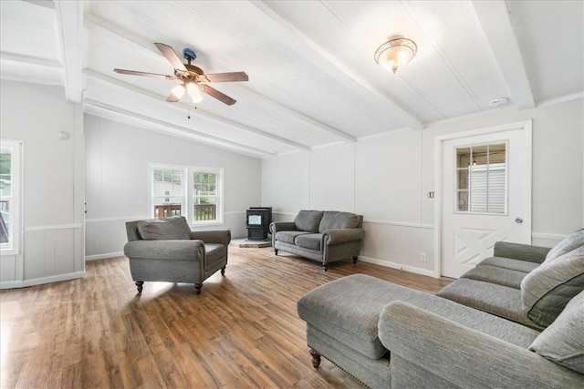 living room featuring vaulted ceiling with beams, ceiling fan, wood-type flooring, and a wood stove