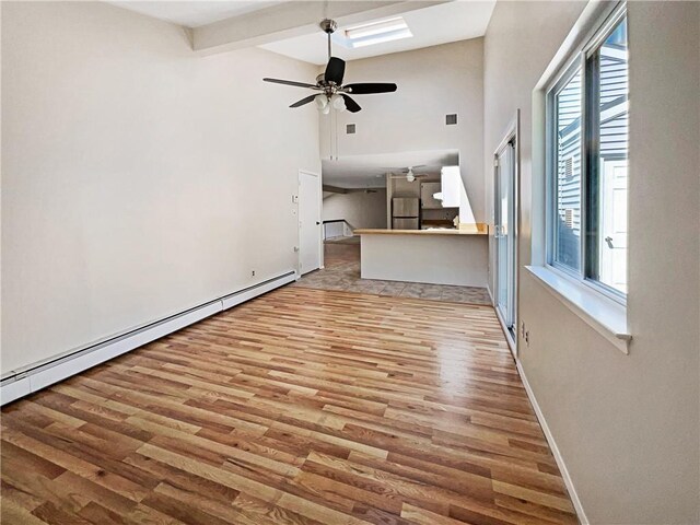 unfurnished living room with a high ceiling, a baseboard heating unit, ceiling fan, light wood-type flooring, and beam ceiling