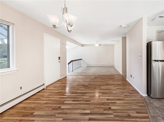 unfurnished dining area featuring baseboard heating, a chandelier, and wood-type flooring