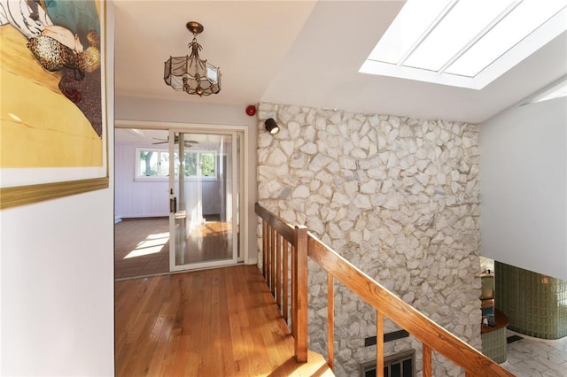 corridor with vaulted ceiling with skylight and wood finished floors