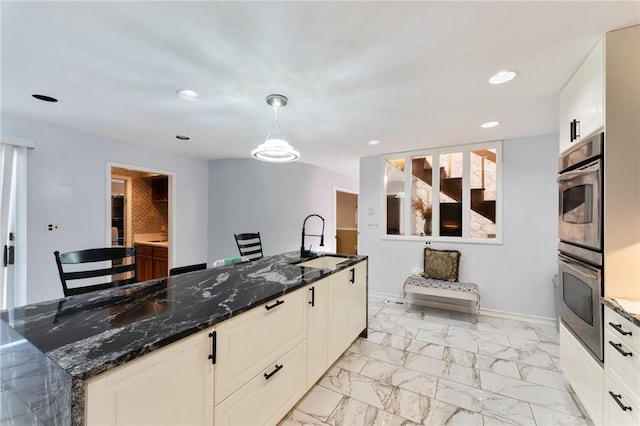 kitchen featuring dark stone counters, marble finish floor, stainless steel double oven, a sink, and recessed lighting