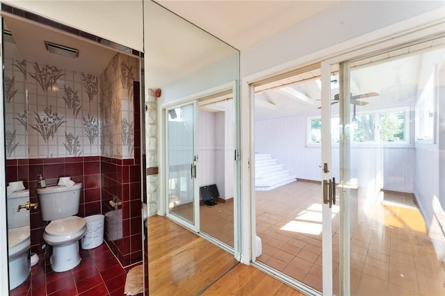 bathroom with a ceiling fan, toilet, wood finished floors, french doors, and tile walls