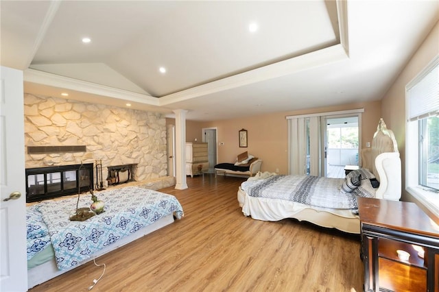 bedroom featuring a tray ceiling, a stone fireplace, wood finished floors, access to outside, and ornate columns