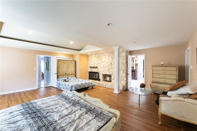 bedroom with a stone fireplace, recessed lighting, wood finished floors, and ornate columns