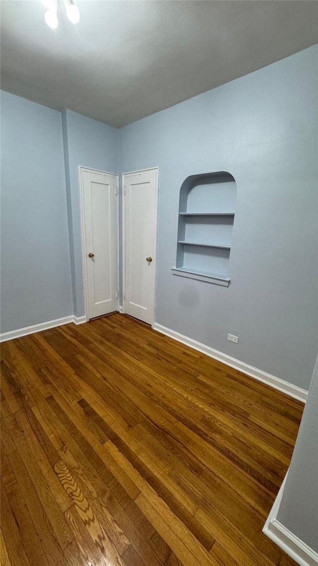 unfurnished room featuring built in shelves and hardwood / wood-style flooring