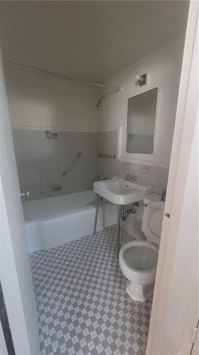 full bathroom featuring tiled shower / bath combo, toilet, tile walls, and sink