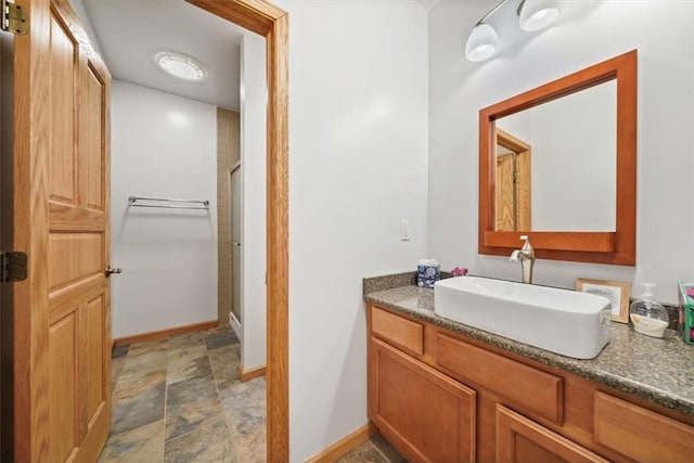 bathroom featuring vanity, a shower with shower door, stone finish flooring, and baseboards