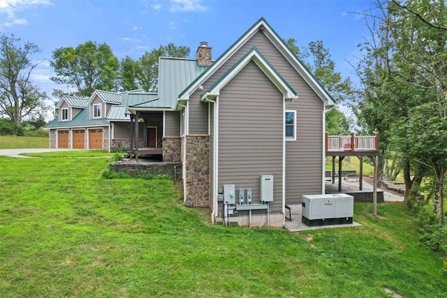 back of property featuring stone siding, metal roof, a chimney, a garage, and a yard