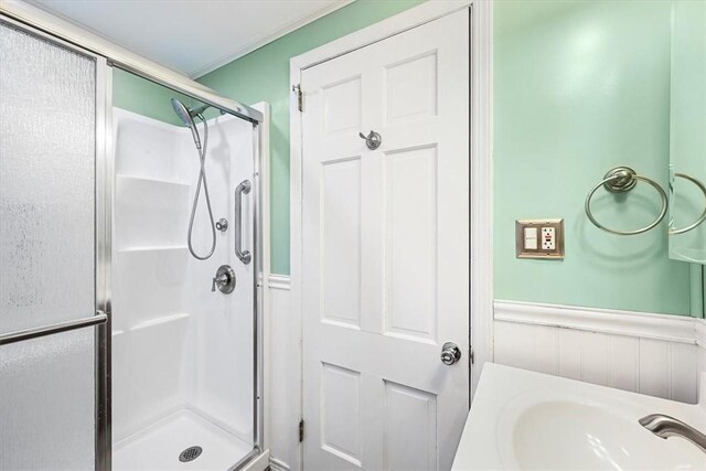 bathroom featuring ornamental molding, a shower with shower door, and sink