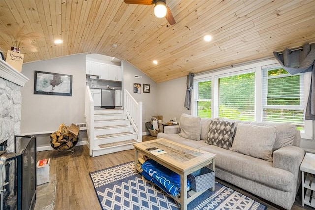 living room featuring wood ceiling, vaulted ceiling, ceiling fan, light hardwood / wood-style floors, and a stone fireplace