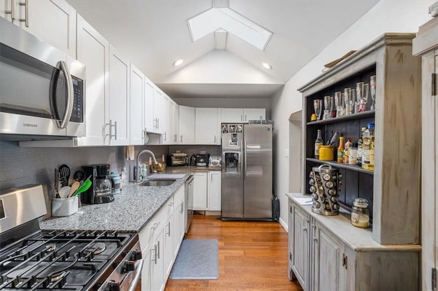 kitchen with lofted ceiling with skylight, white cabinets, light hardwood / wood-style floors, light stone counters, and stainless steel appliances