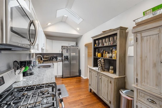 kitchen featuring white cabinetry, vaulted ceiling with skylight, light wood-type flooring, and appliances with stainless steel finishes