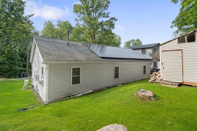 rear view of house with solar panels, an outdoor structure, and a yard