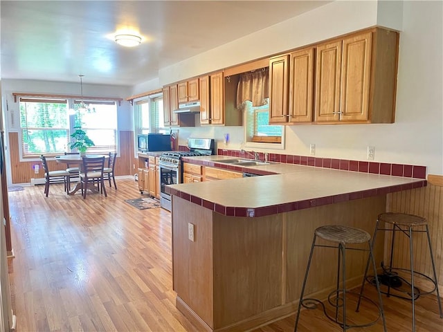 kitchen with kitchen peninsula, light hardwood / wood-style flooring, stainless steel gas stove, hanging light fixtures, and a breakfast bar area