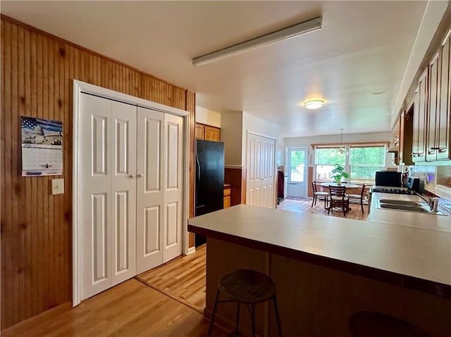 kitchen featuring kitchen peninsula, wood walls, sink, and light wood-type flooring