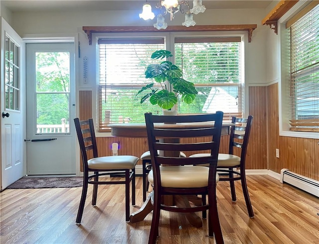 dining area with baseboard heating, wood walls, hardwood / wood-style floors, and an inviting chandelier