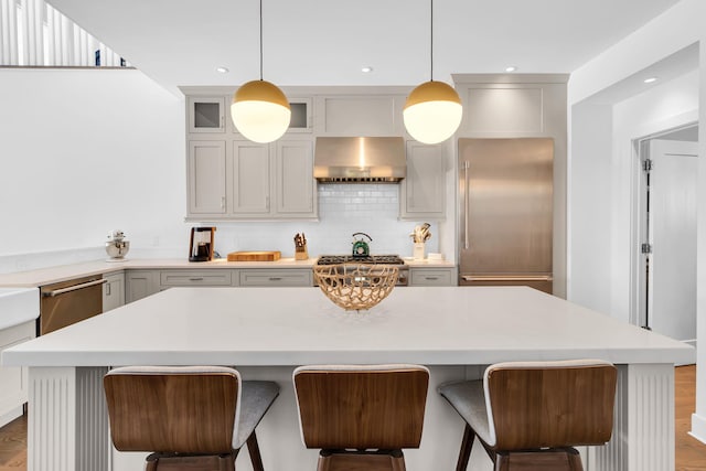 kitchen featuring wall chimney range hood, decorative light fixtures, stainless steel appliances, and a center island