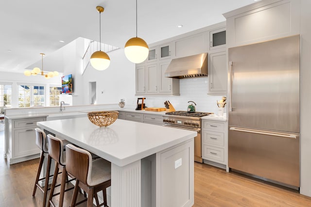 kitchen featuring a center island, high end appliances, a kitchen bar, decorative light fixtures, and wall chimney exhaust hood