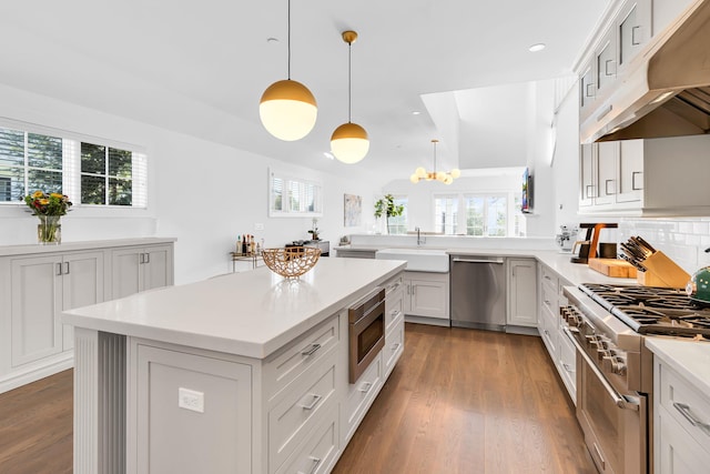 kitchen with hanging light fixtures, a kitchen island, stainless steel appliances, a healthy amount of sunlight, and white cabinets