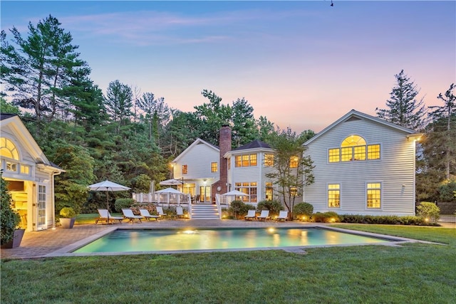 back house at dusk featuring a patio area and a yard