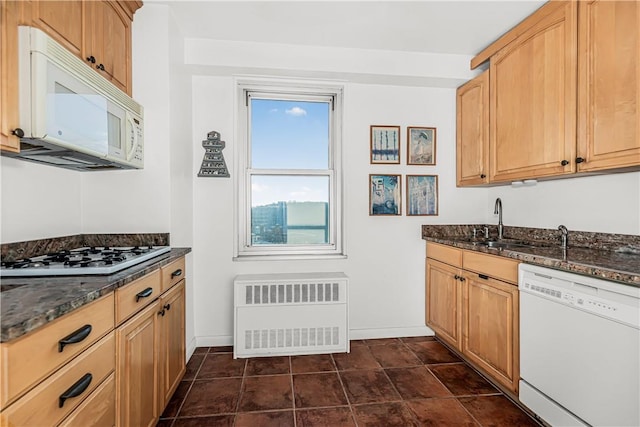 kitchen featuring radiator, light brown cabinetry, dark stone counters, and white appliances