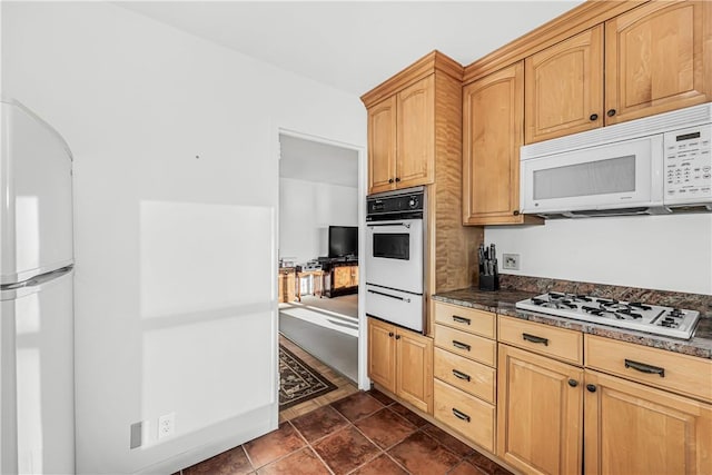 kitchen with light brown cabinetry, dark tile patterned floors, and white appliances