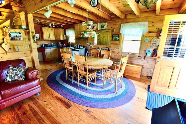 dining area with beam ceiling, wood walls, and light hardwood / wood-style flooring