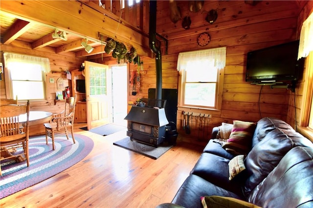 living room featuring a wood stove, wooden walls, beamed ceiling, and light wood-type flooring