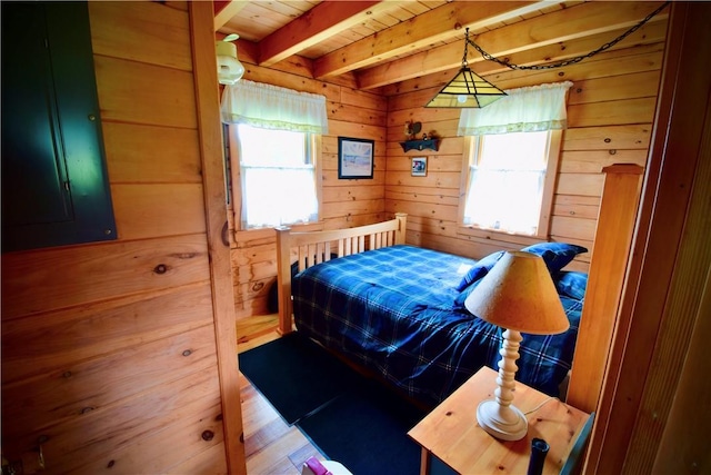 bedroom with hardwood / wood-style floors, beam ceiling, wood walls, and multiple windows