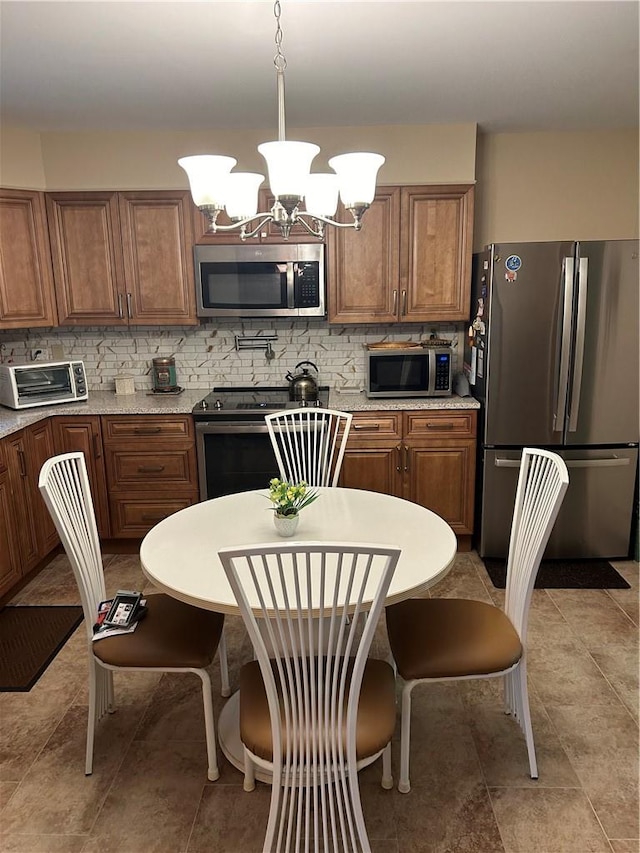 kitchen featuring pendant lighting, appliances with stainless steel finishes, tasteful backsplash, light stone counters, and a chandelier