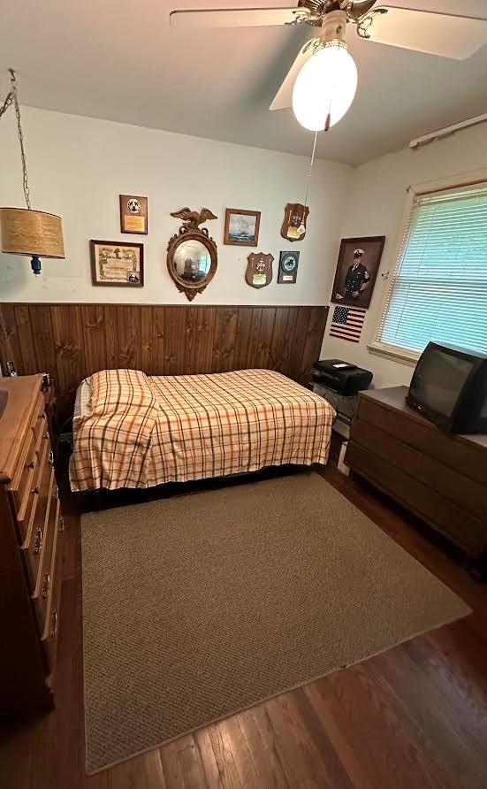 bedroom featuring ceiling fan, hardwood / wood-style floors, and wooden walls