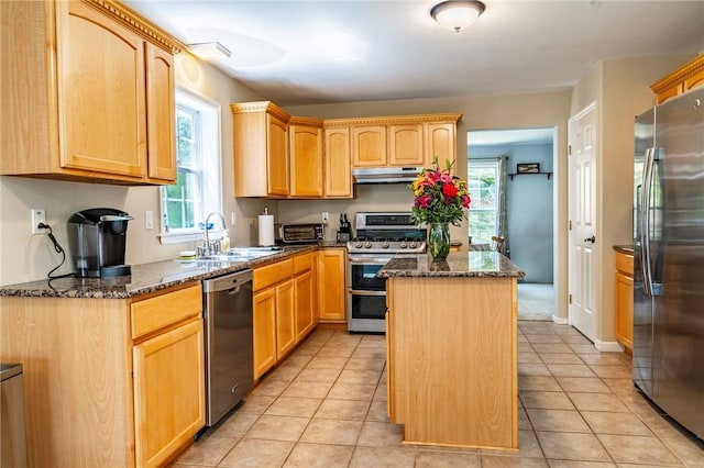 kitchen with dark stone counters, stainless steel appliances, sink, a center island, and light tile patterned flooring