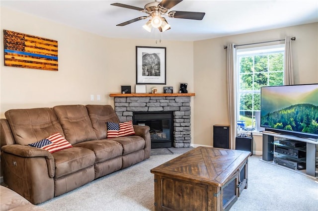 living room featuring a stone fireplace, ceiling fan, and light colored carpet