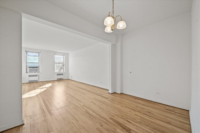 spare room with a notable chandelier, light hardwood / wood-style floors, radiator, and cooling unit