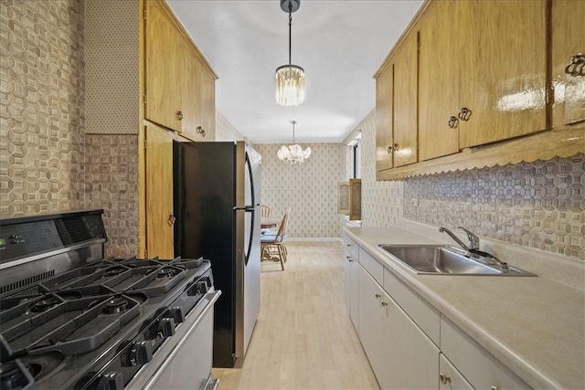 kitchen with pendant lighting, sink, appliances with stainless steel finishes, a notable chandelier, and light hardwood / wood-style floors