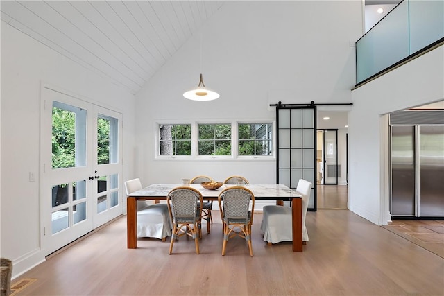 dining space with a barn door, french doors, high vaulted ceiling, and hardwood / wood-style floors