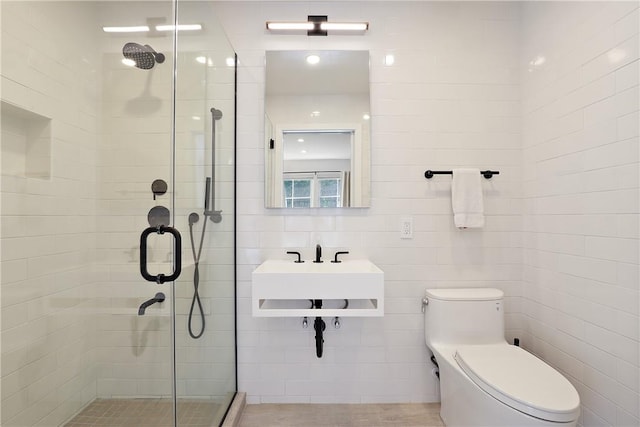 bathroom featuring sink, a shower with door, tile walls, and toilet