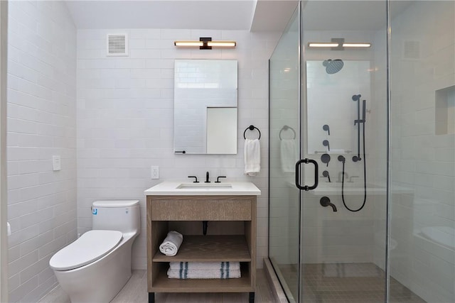 bathroom with vanity, toilet, a shower with door, and tile walls