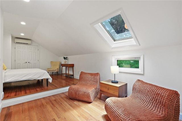 bedroom featuring a wall mounted air conditioner, light hardwood / wood-style floors, lofted ceiling with skylight, and a closet