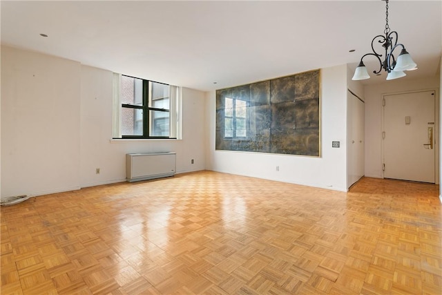 spare room with radiator, light parquet flooring, and an inviting chandelier